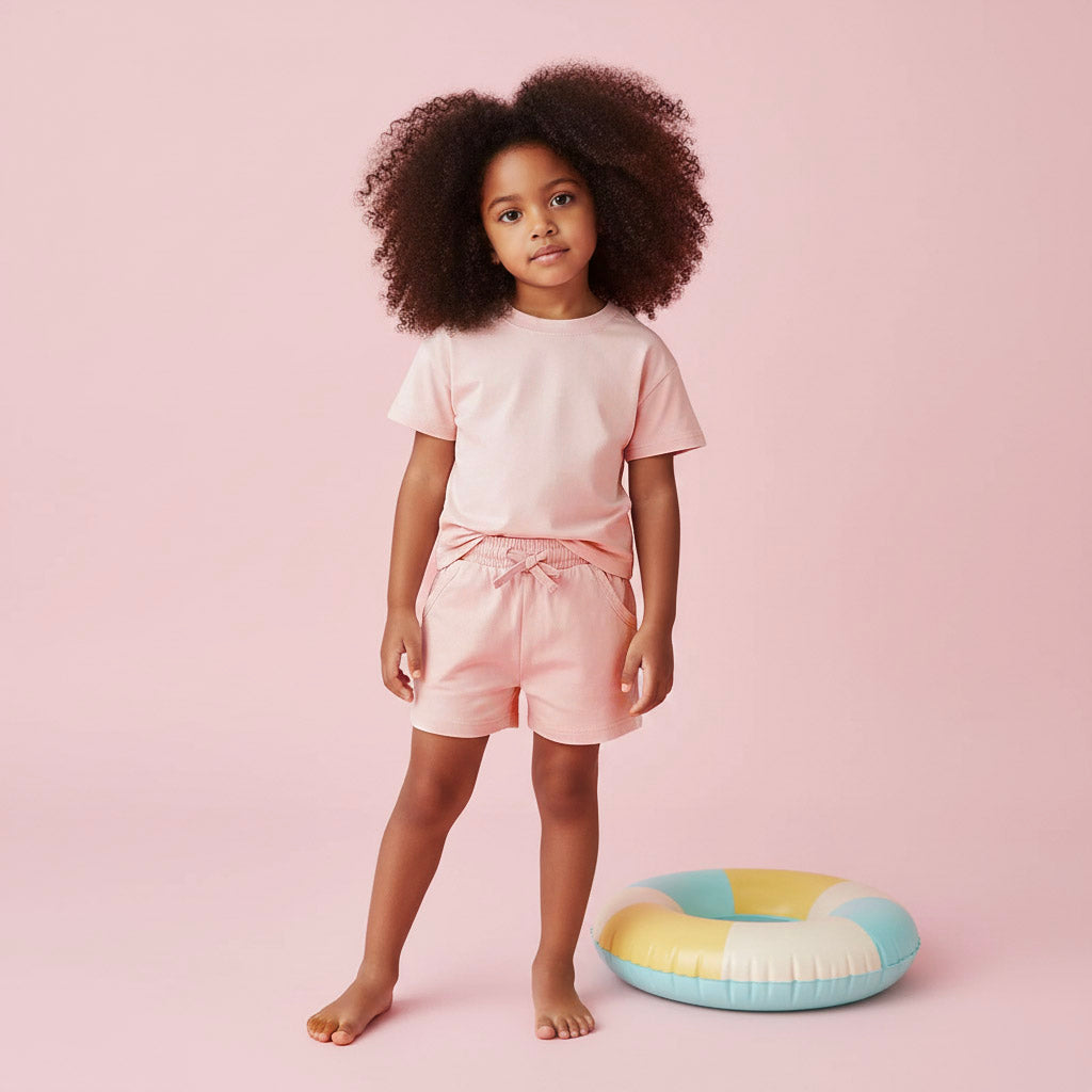 Child wearing a pink outfit standing next to a colorful inflatable ring on a pink background
