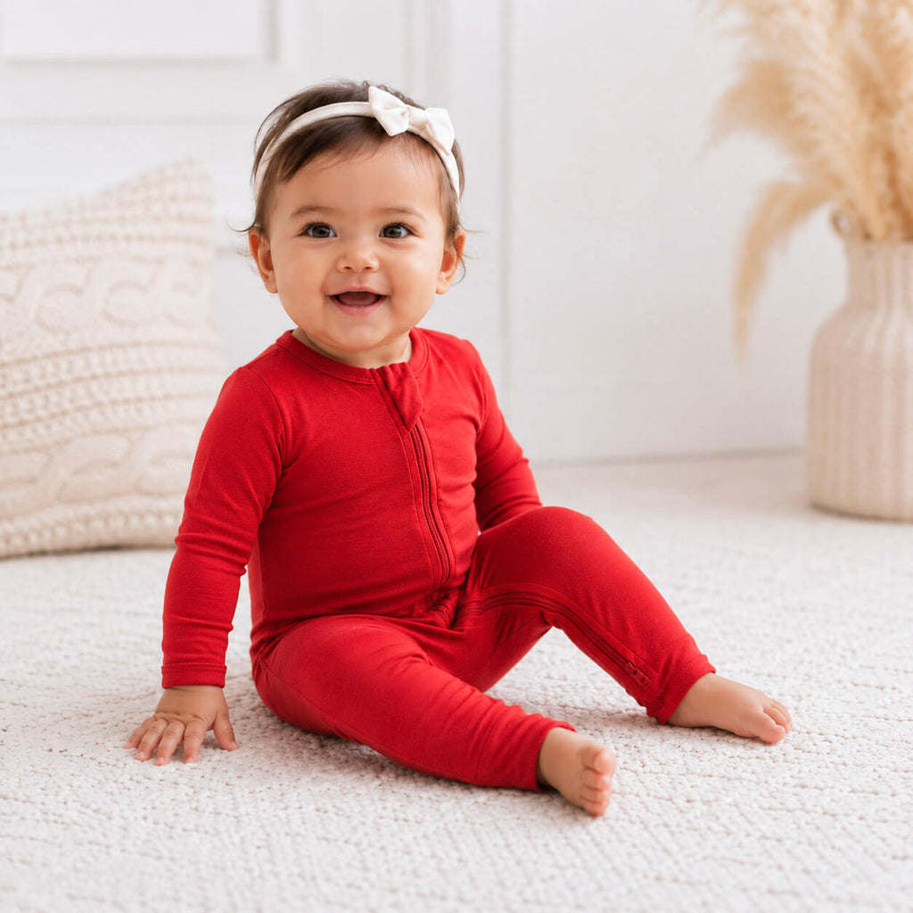 Baby in a red onesie sitting on a white surface with a neutral background