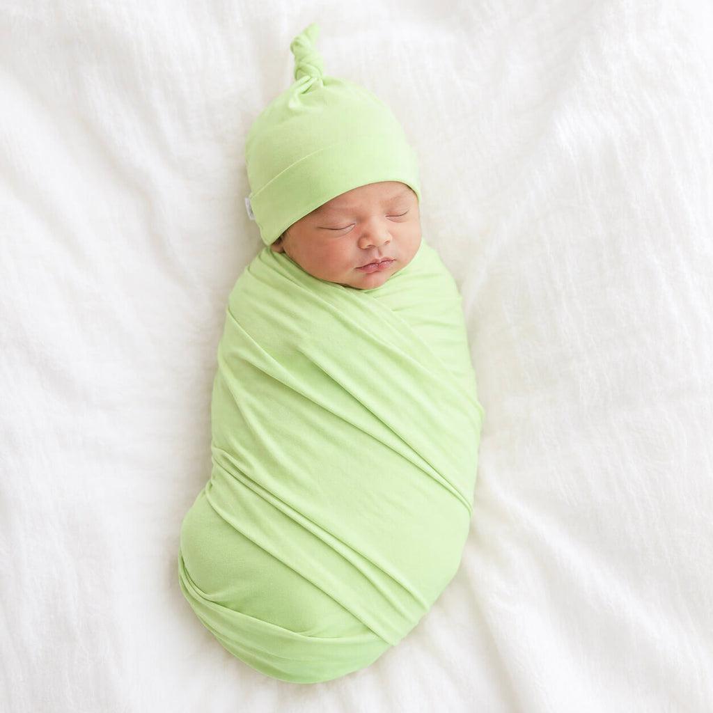 Newborn baby wrapped in a green swaddle and hat on a white background