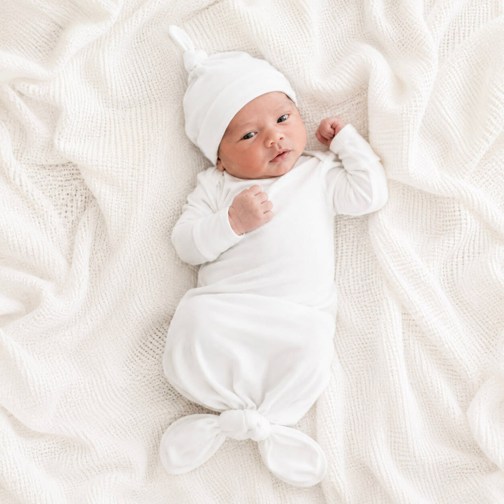 Newborn baby wrapped in white gown and beanie on a soft white blanket