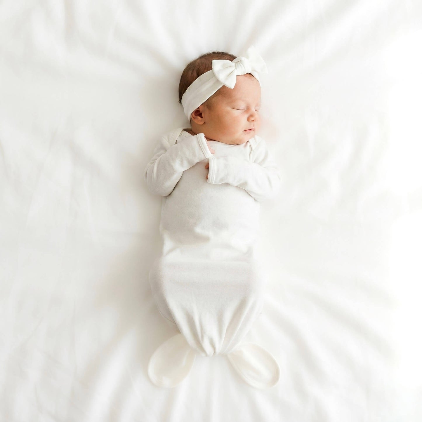 Newborn baby wrapped in white with a headband on a white background