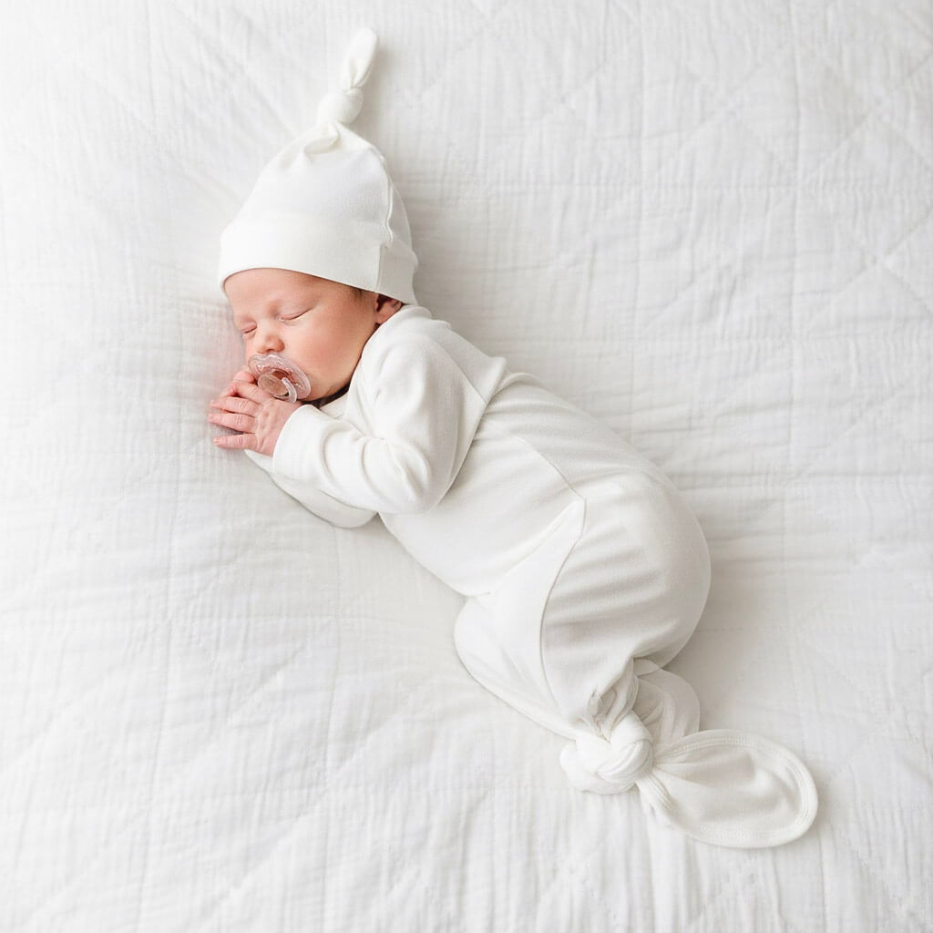 Newborn baby swaddled in white with a matching hat on a white blanket