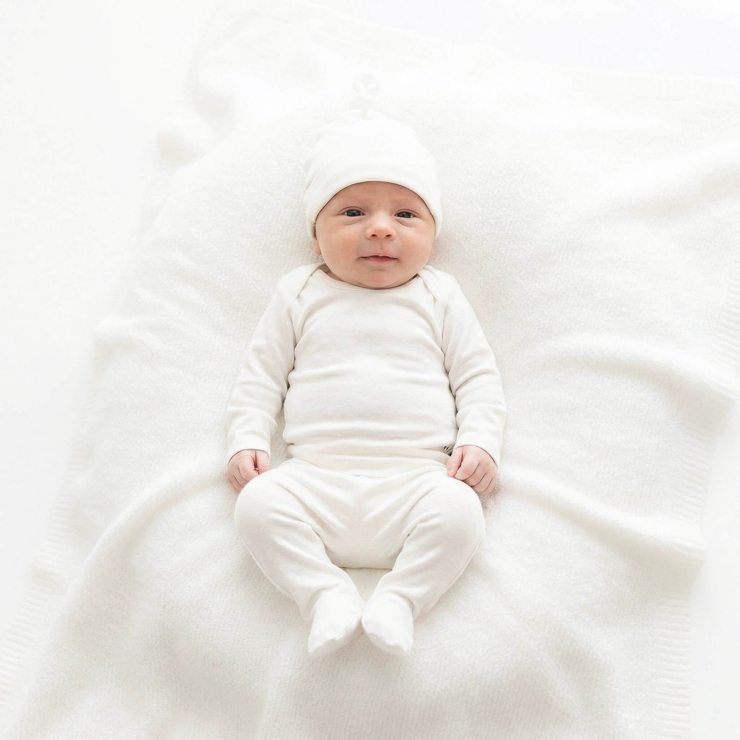 Baby in a white outfit lying on a white blanket