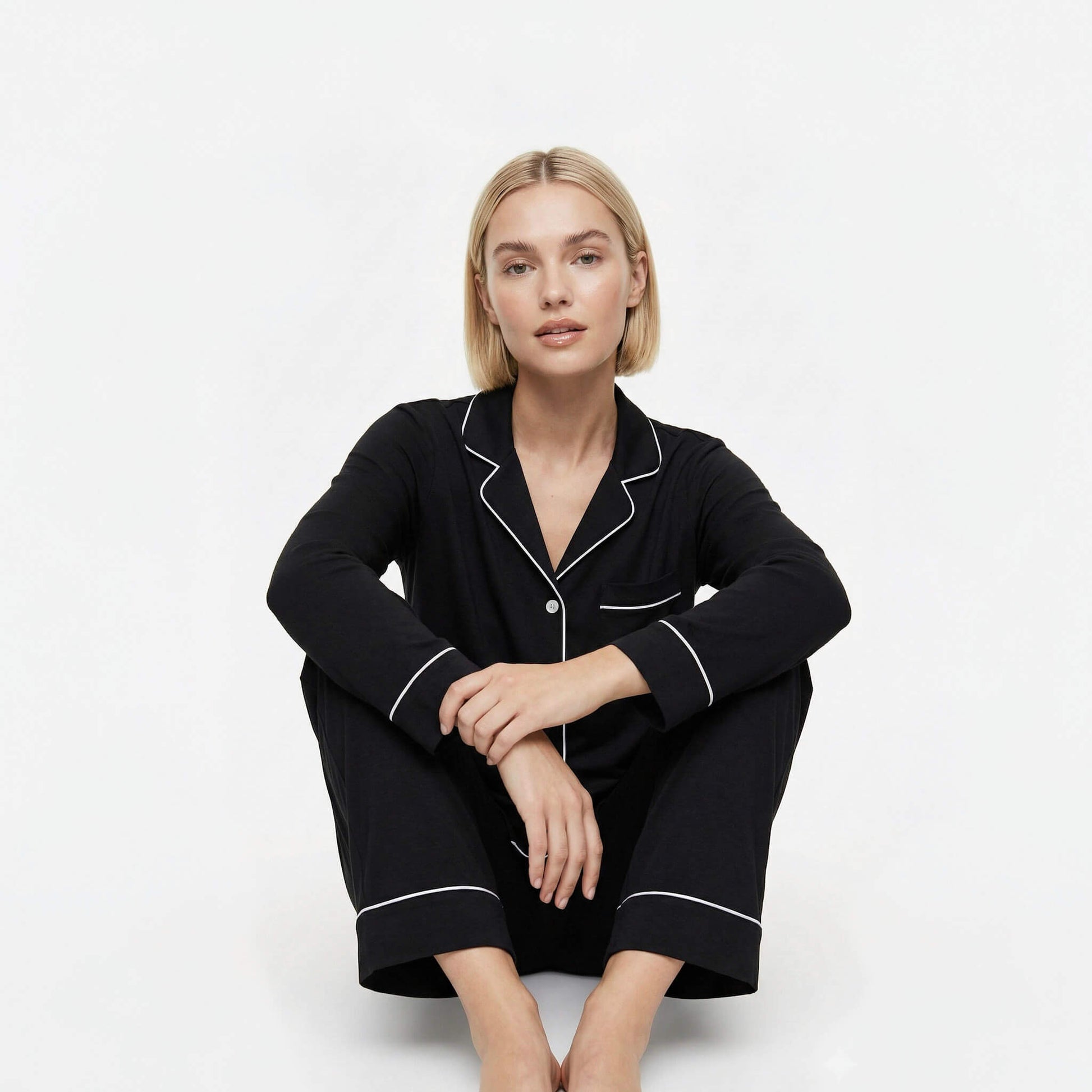 Woman wearing black pajamas with white piping on a white background