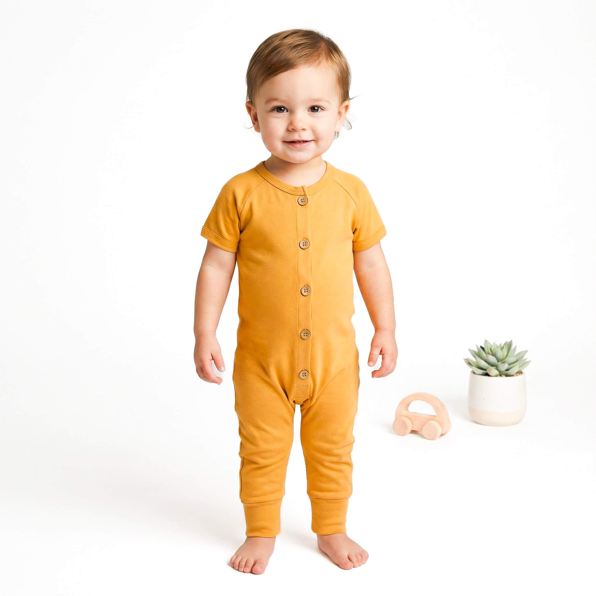 Baby wearing a mustard yellow onesie on a white background